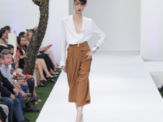 Modella con camicia bianca e pantaloni a vita alta color cammello.