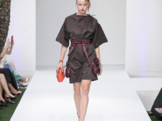Modella con mini-abito marrone e borsetta arancione.