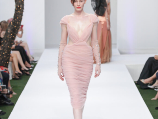 Modella con un abito rosa cipria drappeggiato e guanti trasparenti.