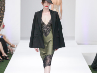 Modella con abito verde in pizzo nero, blazer nero e copricapo.